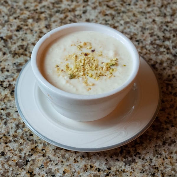A white bowl of creamy Indian rice pudding, kheer, topped with chopped pistachios on a granite surface.