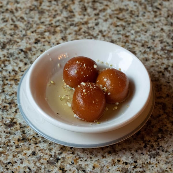 Three gulab jamun, Indian fried dough balls in syrup, sprinkled with nuts in a white bowl.