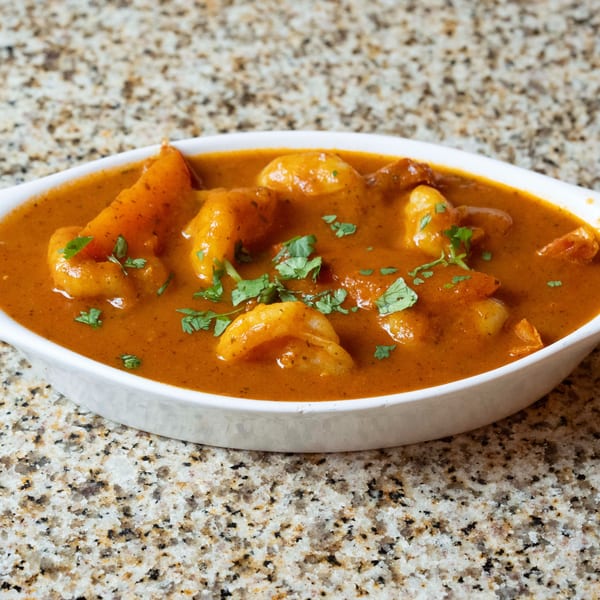 A white oval dish filled with Indian shrimp curry, garnished with fresh cilantro, on a granite countertop.