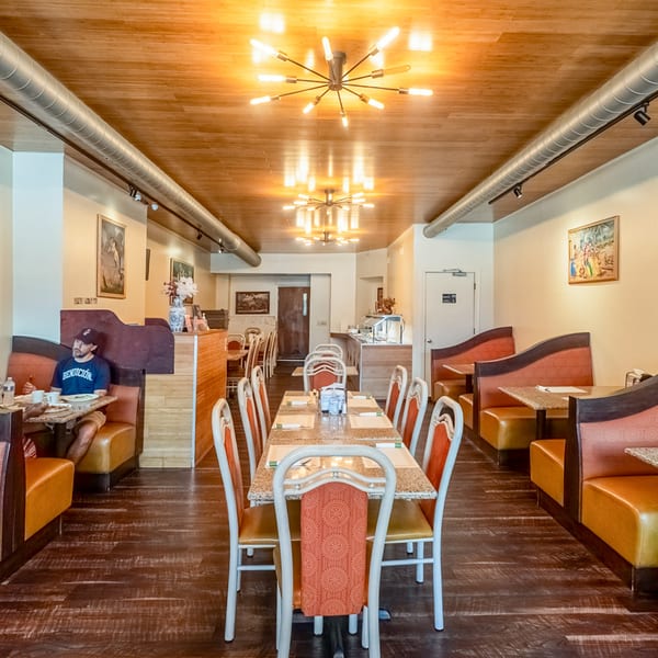 Taste of India dining room with a long table, booths, and a man seated at a table.