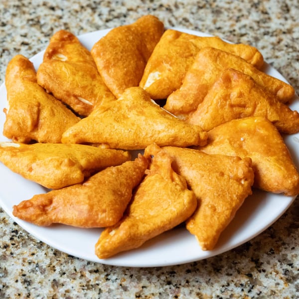 A white plate filled with golden-brown, triangular Indian paneer pakora, on a speckled countertop.