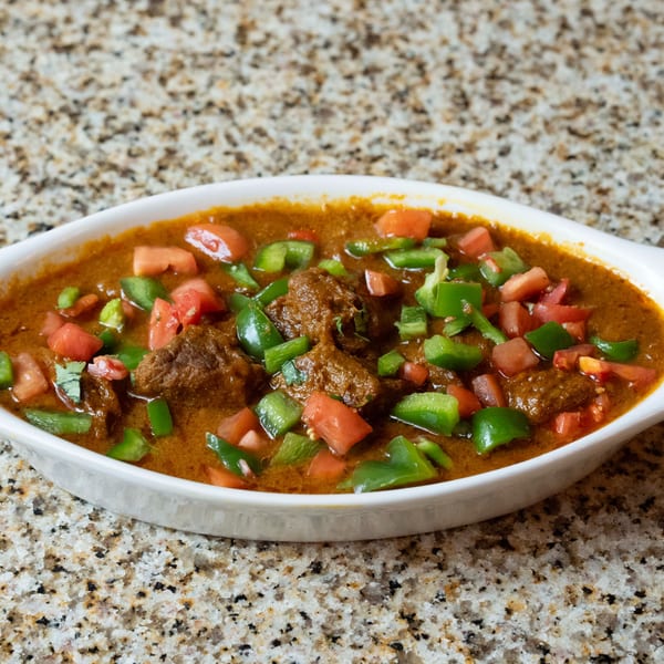 Indian curry with meat, diced tomatoes, and green bell peppers in a white dish.