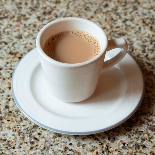 A white mug of Indian chai tea with a foamy top, on a matching saucer and granite surface.