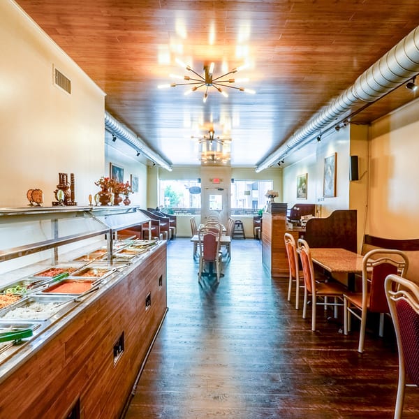 Interior of Taste of India restaurant with a buffet line, tables, chairs, and modern lighting.