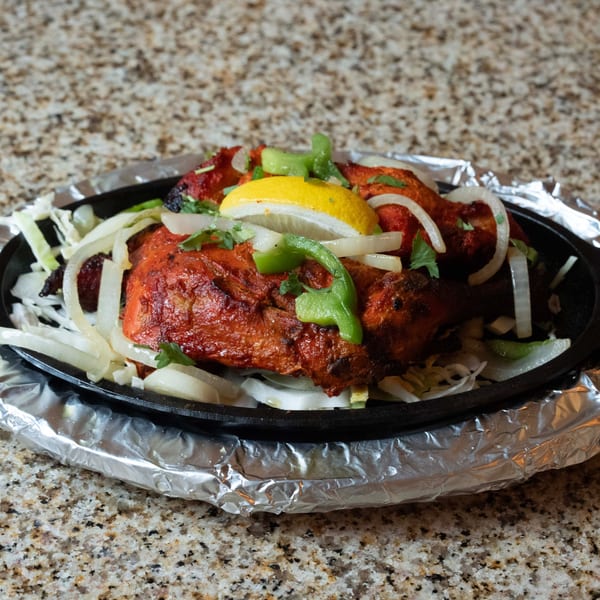 Indian Tandoori Chicken, garnished with lemon, onions, and green peppers, served on a hot plate.