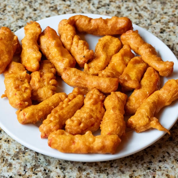 A white plate filled with golden-brown, crispy Indian pakora, a fried snack, on a speckled countertop.