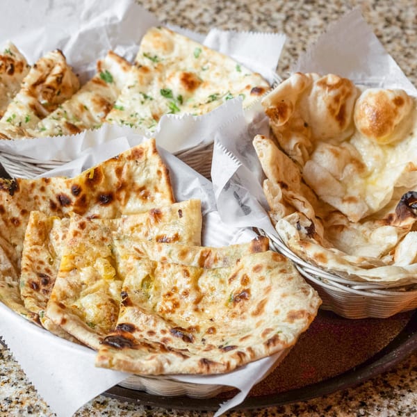 Baskets of freshly baked Indian naan bread, some plain, some with herbs, on a granite surface.