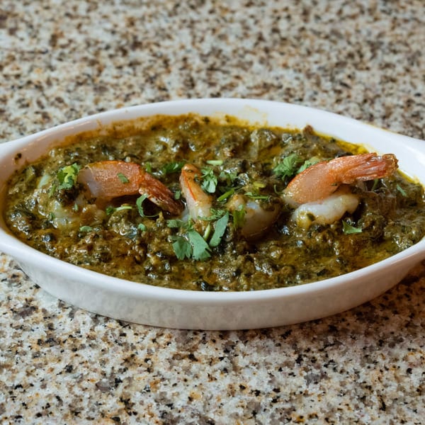 Indian shrimp palak curry, garnished with cilantro, in a white oval dish on a granite counter.